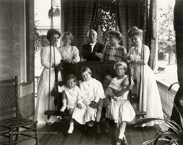 Portrait of family on a porch; adults are standing and children are sitting on a porch swing.