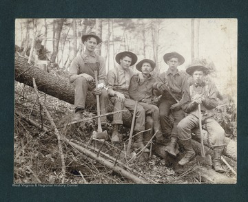Five men sit on a fallen tree.  John Swisher is seated in the middle.  The man seated on the far right, on the lower end of the fallen tree, is possibly William Vernon Riley.  The man seated second from the far right, and second from the end of the lower part of the fallen tree, is possibly William Vernon Riley's brother, Harry Vincent Riley.
