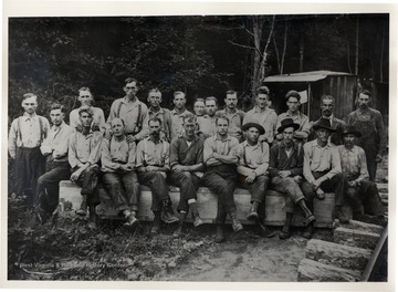 Group portrait of men sitting on a wooden bench.<br />