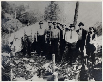 Group of men pose at their camp site. None are identified.