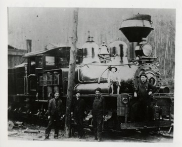Four men and a boy pose beside and on a train engine.  
