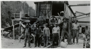 Group portrait of lumber crew, mill in background. 
