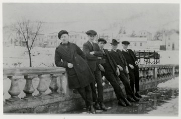 Five men leaning on a cement bridge looking west.  Town in the background.  