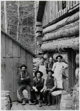 Six men in front of a log camp building, early 1900s or before.