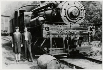 Man and girl standing beside a Shay train engine.  