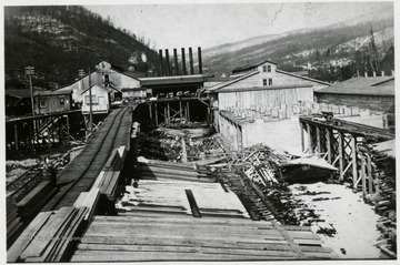 Lumber mill, train tracks, 6 smoke-stacks, and lumber piles.