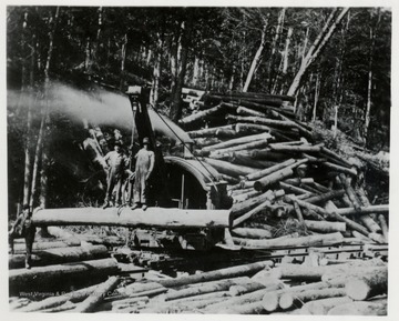 Two men standing on a log being lifted up by a loader.