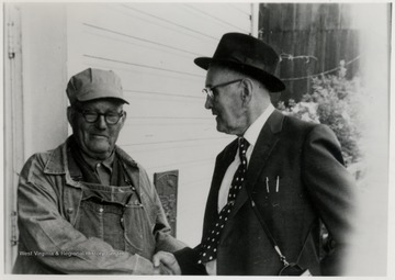Two men shaking hands.  One man is wearing a conductor hat.  