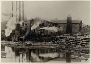 Lumber mill in operation on edge of log pond.