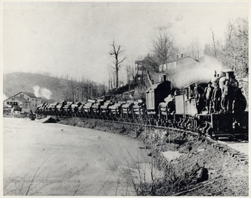 Men stand on a Shay locomotive hauling a train of cars filled with logs.