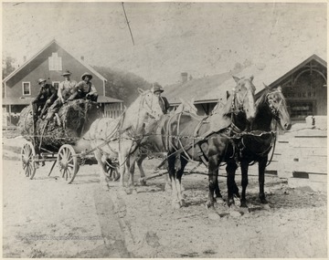 Four horses pulling a large log.   Neither the store nor the railroad building are still standing today.