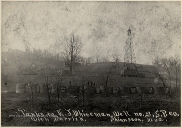 Men stand atop oil tanks with derrick in the background.