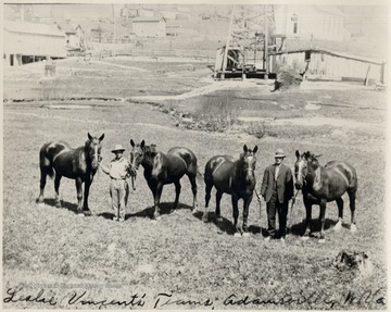 Two men standing with four horses.  Oil well in background.