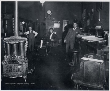 Three men posed in an unidentified Oil and Gas Company office. Decorative gas stove in foreground. 