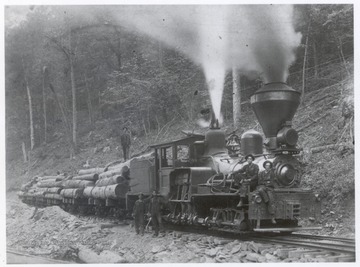 Train engine carrying a cart of logs.  Crew members pose for photograph.