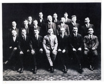 The following caption appeared under the picture in a clipping from the Weston Democrat, undated. 'The men who founded the modern glass industry in Weston are seen in this old photo, loaned to us by Mat Holt. Front row, left to right, Frank Model, Henry Model, Elglebert Hager, Louie Wohinc, Mr. Lawrence, Karl Wohinc, and Louie Schrader. Second row, left to right, Henry Tomasche, John Pertz, Godfrey Weber, Dr. M.S. Holt, Joe Hager, Rudolph Bauer, and Frank Lanhanse. Third row, left to right, John Weber, Jumbo Ransinger, Ed Bascisko, and August 'Gus' Weber. Most of these men were employed in the glass factory at Tennerton. About 1920 a bottle factory at Weston closed. It was located where the Mountaineer Glass Company is now. Dr. Holt, who was the physician to most of the families, bought for them the old bottle plant for about $15,000. He was the only stockholder who was not a worker in the plant. Mr. Lawrence was the office manager and bookkeeper. The factory was organized with a $50,000 capital. Elglebert Hagar was the first president and general manager.' 