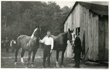 Men show their horses next to a barn.