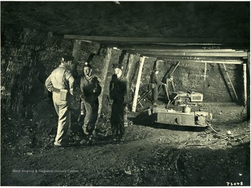 Miners talking while others run drilling equipment.