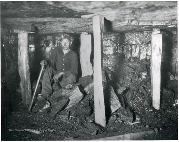 Miner sitting in between posts that hold the roof of the mine up. 'Safety First is stressed in every possible way at White Oak mines.  Note the posts to protect this man at his labor.  He is waiting for another mine car so he can clean up his working place and make it ready for the mining machine crew who will cut it during the night, ready for him to work tomorrow.'