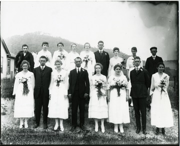 Group portrait of girls in white dresses with bouquets attached in front and boys in dark suits.