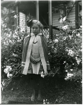 Grace Holtkamp (Herrstrom) standing in the middle of flowers.  House in the background.  Helvetia, W. Va.