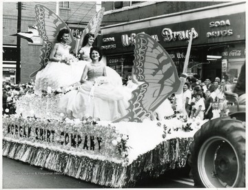 Three ladies in white dresses ride on the Morgan Shirt Company float.