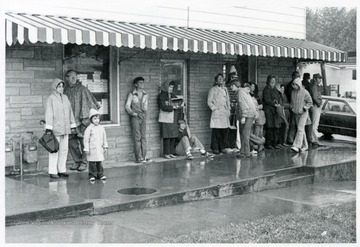 A group of people stand under an awning to watch the parade.