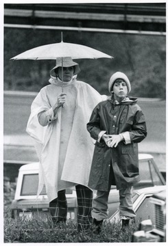 A lady holding an umbrella stands with a boy.