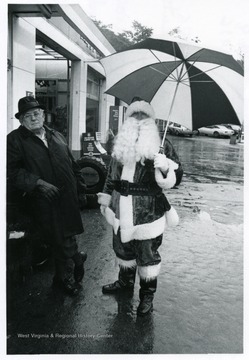 A man dressed like Santa Claus holds an umbrella.