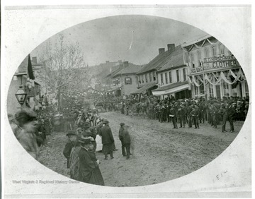 Townspeople are watching a parade at the corner of High and Walnut Streets in Morgantown, West Virginia.