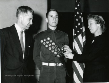 Mrs. Garlow pins an Eagle Scout award onto son David's sash while his father John looks on.