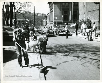 Construction workers are working at the corner of High and Spruce Streets in Morgantown, West Virginia. 'Lower left: John Mollennex, West Virginia University student from Elkins. The Post Office is in the background.'