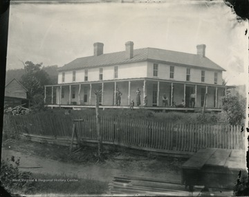 A view of a residence enclosed by a wooden fence at Jackson's Mill with people sitting and standing on the porch.