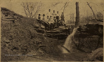 Group of students in a medical class pose by a small water fall near Falling Run, some are wearing long aprons; on the site now stand Business and Economic and Life Science Buildings. An inscription of 'Dr. J.F. Trippett died August 20, 1912' with a signature of Clyde Trippett, M.D. on the back.