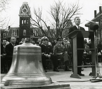 Military officers listen as Joseph Gluck speaks at dedication of the bell from the 'West Virginia' outside Oglebay Hall. In the background is Woodburn Hall. 