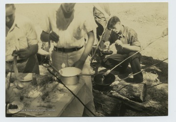 Boys appear to be cooking on sticks and in a pan over a fire.