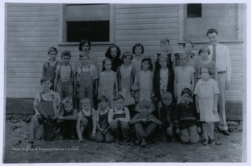A group of Fletcher School students stand in front of the school house with their teacher, Joseph Lyons.