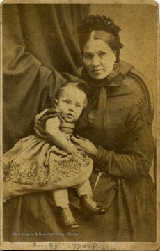 A carte de visite photograph of a woman holding a small child. There is a federal revenue stamp on the back of the photograph, indicating a tax had been paid on the image. This stamp tax was passed by Congress to pay for raising costs of the Civil War from 1864 to 1866.