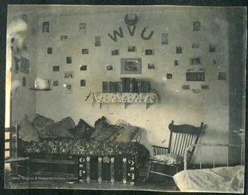 Room walls decorated with photographs and "WVU" . Two steamer trunks covered with a blanket and pillows.