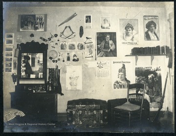 Room furnished with a dresser/wash stand, a trunk and a cadet's rifle in the corner. The walls decorated with posters, calendars, and memorabilia.