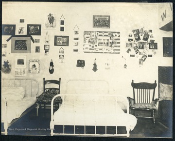 Furnishings include white metal framed beds, a rocker and walls decorated with students' memorabilia and photographs.