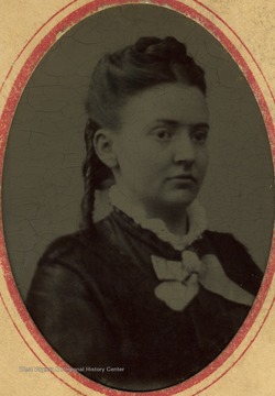 A young woman wearing curls and a with a high collar. Inscription on front and back, "Compliments of Nora V. Kauntz".