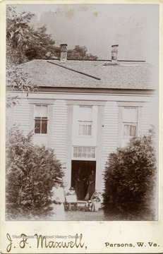 Rufus Maxwell and his wife Sarah Bonnefield Maxwell sit outside by the front open door, others are not identified. Photo taken at the old Maxwell home.