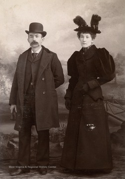 A cabinet card photograph of a couple waering the fashions of the day including hats.