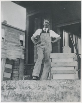 Loomis pictured in overalls standing next to wooden crates. 