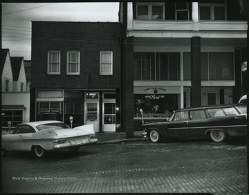 Cars are parked along the street in front of store buildings. Hinton Floral Shop and The Chesapeake and Potomac Telephone Company are pictured. 