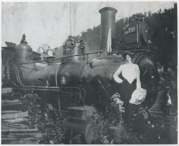 Mary Murrell, married to R. O. Murrell, poses beside the engine. 