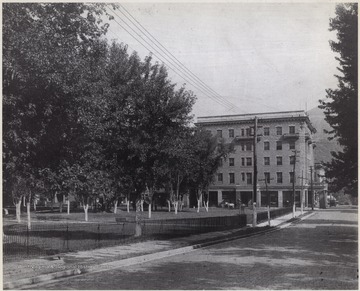 The square, to the left, is comprised of scattered trees and park benches. In the background is McCreery Hotel.