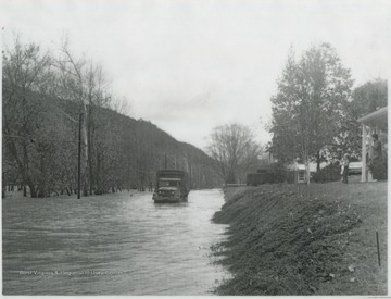 A United States National Guard truck attempts to make its way across the flooded Greenbrier Drive as a young boy and man watch from their home above. Subjects unidentified. 