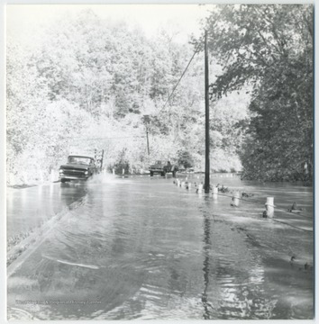 Two cars are seen splashing through the waters of the gradually submerged road.